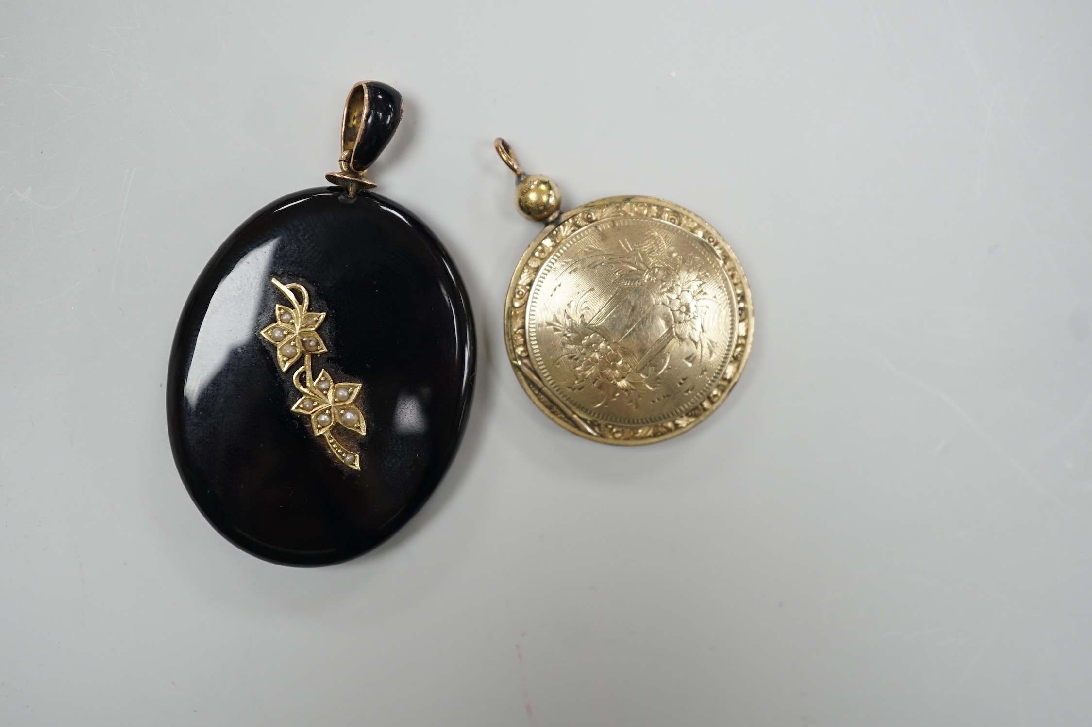 A Victorian yellow metal and seed pearl mounted black onyx oval pendant locket, with enamelled bale, overall 53mm and an engraved gold plated circular pendant locket.